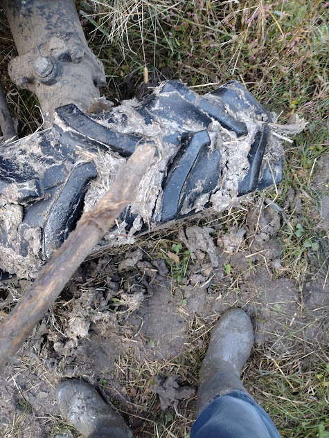 前進で引き出しを試みるトラクターの泥に灌水ポンプの水流を当てた後に枝木で詰まった残りの泥を出そうとする様子