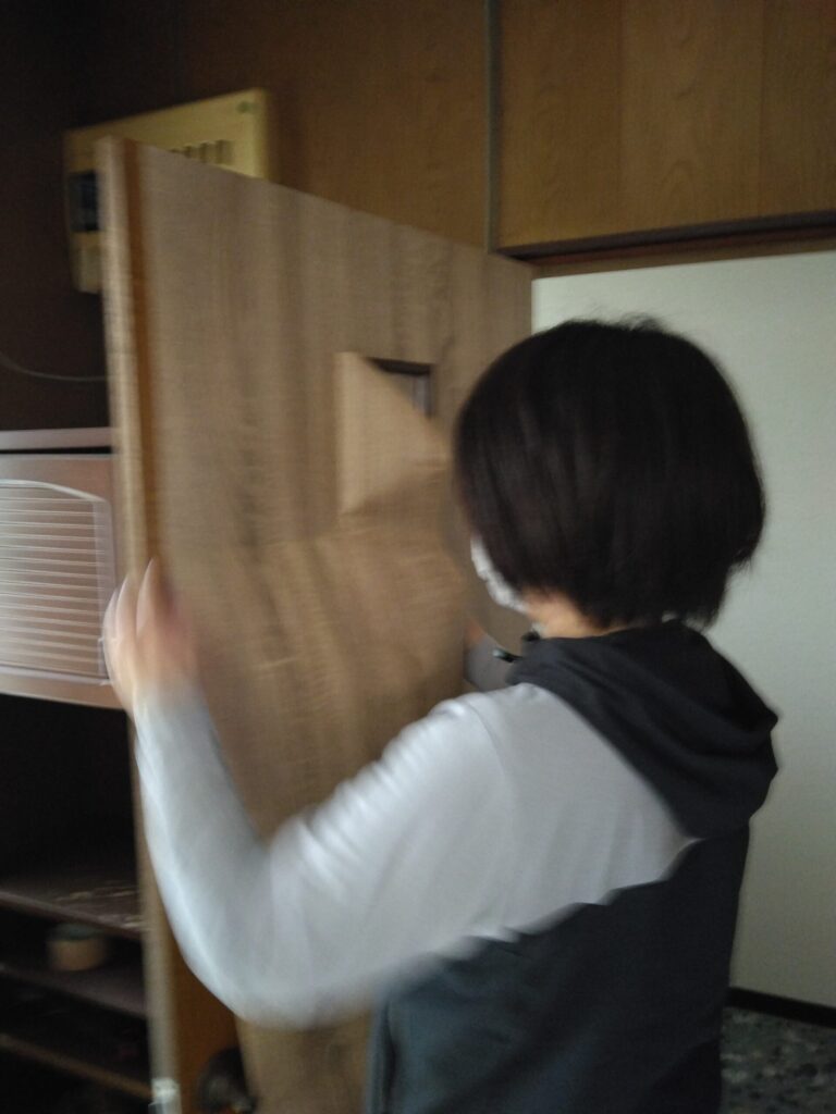 妻がトイレドアに手際よくロール状リメイクシートを貼っていきます。
