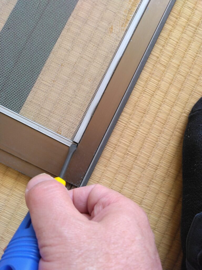マイナスドライバーで網戸の留め具をの取っ掛かりを引き上げます